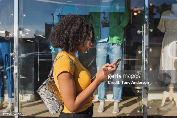 young woman looking at phone outside shop window - a la moda stock pictures, royalty-free photos & images