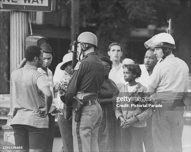 Armed state police officers talking with a group of people, cautioning them to leave the streets ahead of the curfew in the wake of the 1967 Detroit...