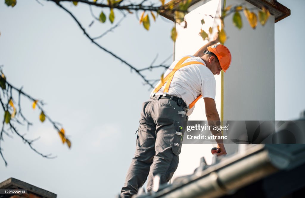 Roofer measuring chimney on roof top