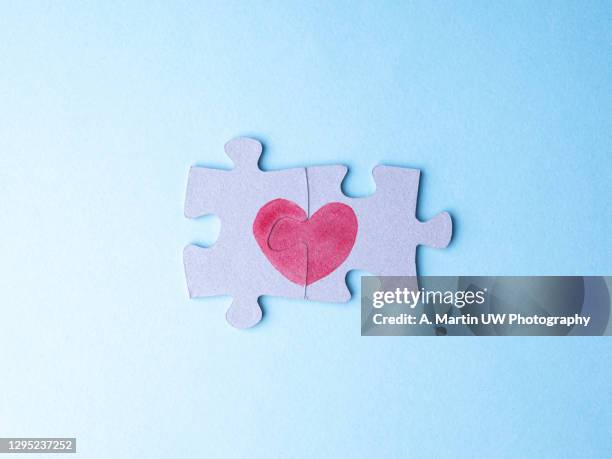 closeup of two pieces of a puzzle forming a heart on a blue background. - two hearts stock pictures, royalty-free photos & images