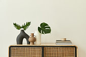 Modern scandinavian home interior with design wooden commode, tropical leaf in vase, books and personal accessories in stylish home decor. Template. Copy space. White walls.