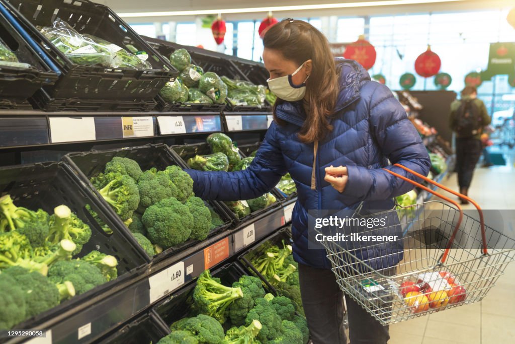 Young woman shopping for healthy food in supermarket with protective facemask