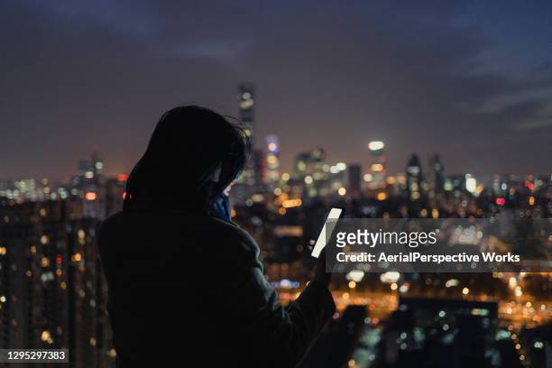 donna che usa lo smartphone sul tetto del grattacielo di notte - big tech foto e immagini stock