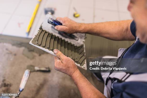 man spreads the surface of the tile with cement adhesive mass using a special hand tool - glue stock pictures, royalty-free photos & images