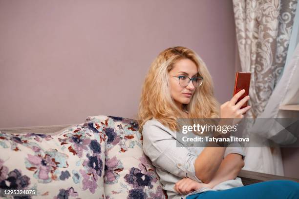 blond curly hair woman looking at smartphone with thoughtfulness expression on face - surprised woman looking at tablet stock pictures, royalty-free photos & images