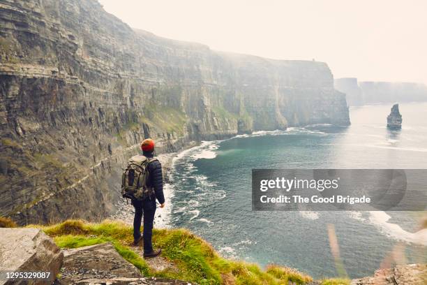 backpacker standing at the edge of the cliffs of moher, galway, ireland - irishman stock-fotos und bilder