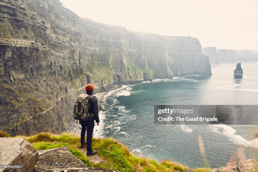 Backpacker standing at the edge of the Cliffs of Moher, Galway, Ireland