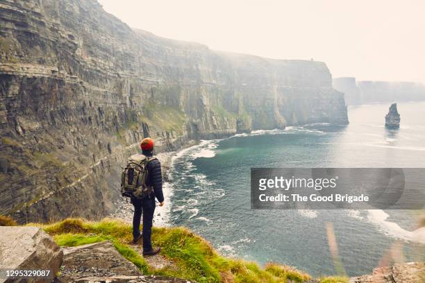 backpacker standing at the edge of the cliffs of moher, galway, ireland - ireland stock pictures, royalty-free photos & images
