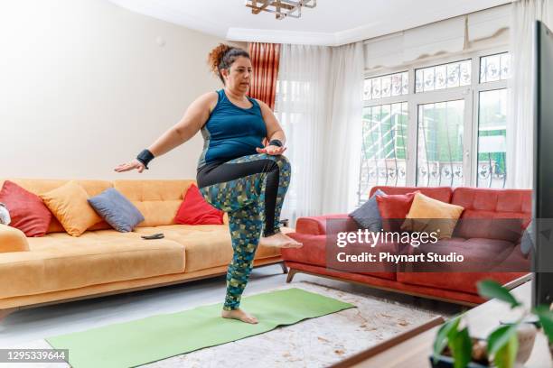 attractive overweight woman at home, tv in front of her, working out  according to video - big fat women stock pictures, royalty-free photos & images