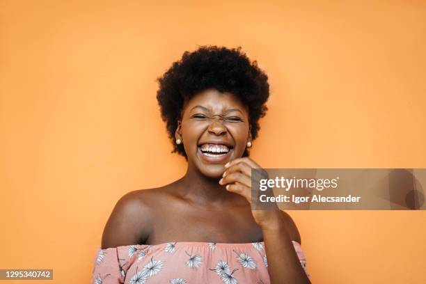 smiling black young woman at orange wall - one woman only laughing stock pictures, royalty-free photos & images