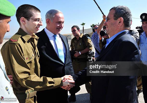 In this handout photo provided by the Israeli Defence Force, freed Israeli soldier Gilad Shalit shakes hands with Defence Minister Ehud Barak next to...