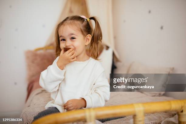 little cute girl eating chocolate in bed - chocolate face stock pictures, royalty-free photos & images