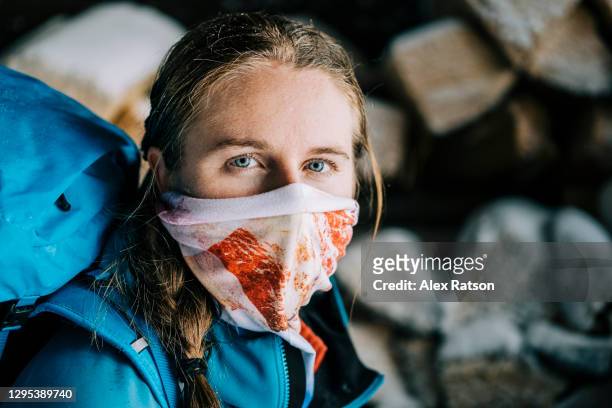 female backcountry skier stands in front of firewood pile waring neck gaiter as a face mask - buff photos et images de collection