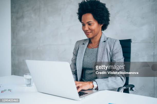 successful businesswoman in modern office working on laptop. - woman in black suit stock pictures, royalty-free photos & images