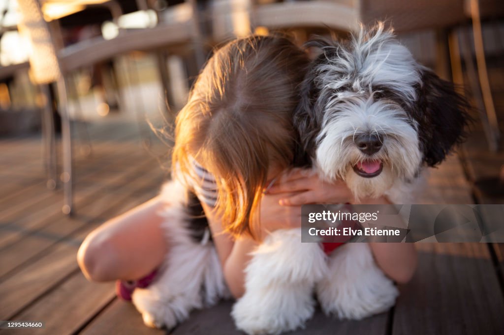 Child hugging young Havanese dog next to an outdoor dining area at a summer holiday villa