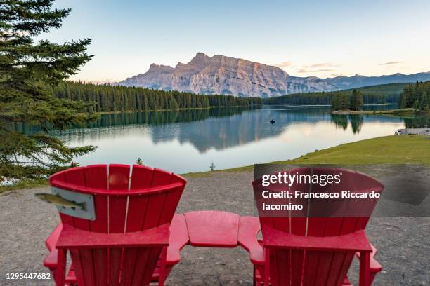 two jack lake and mount rundle reflection in canada at sunset with two red chairs on foreground - lake minnewanka stockfoto's en -beelden
