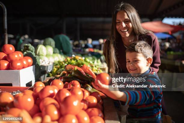 un chico lindo eligiendo verduras con su mamá - mercado de productos de granja fotografías e imágenes de stock
