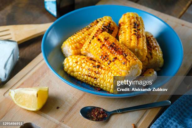 yellow corn cobs, grilled, sprinkled with spices on a bright ceramic plate, against the background of a wooden kitchen table. the concept of homemade food. - roasted corn stock pictures, royalty-free photos & images