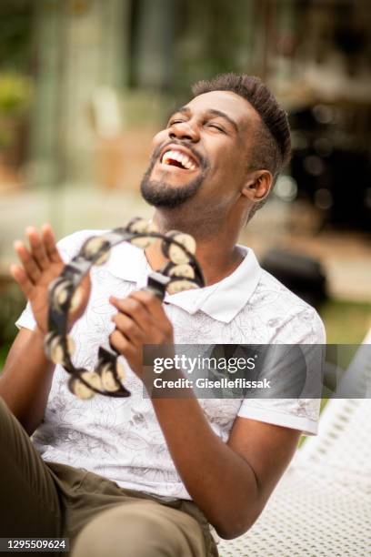 jeune homme riant jouant un tambourin dehors - instrument à percussion photos et images de collection