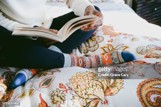 woman relaxes in bed reading book - la casa imagens e fotografias de stock