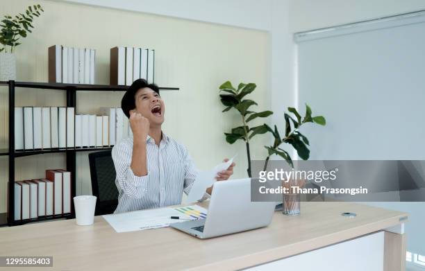handsome young businessman doing a fist pump while working on a computer in an office - punching the air stock pictures, royalty-free photos & images
