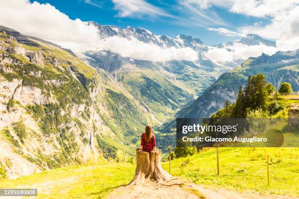 young woman sitting on a tree trunk and admiring the view from murren, switzerland, europe - lauterbrunnen stock pictures, royalty-free photos & images