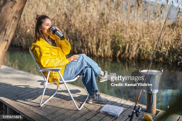 young woman drinking coffee after trying to catch a fish - camping chair stock pictures, royalty-free photos & images