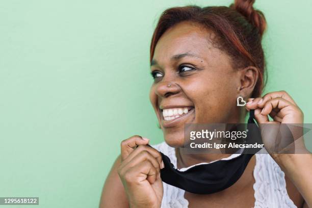 smiling woman taking off protective mask - anti racism masks stock pictures, royalty-free photos & images
