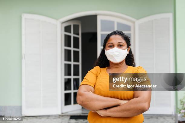 donna seria che indossa una maschera protettiva davanti a casa - persona di casa foto e immagini stock