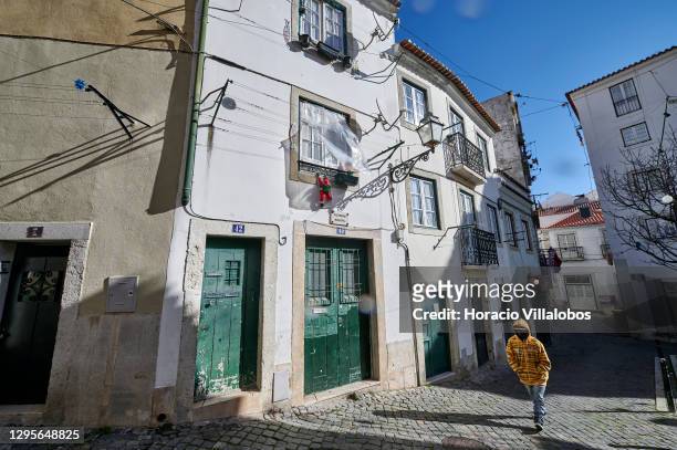 Person wearing a mask walks alone in a deserted street of Alfama historical quarter during the coronavirus pandemic on January 10, 2021 in Lisbon,...