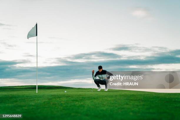 male golfer lining up ball and flag against sky - golfer putting stock pictures, royalty-free photos & images