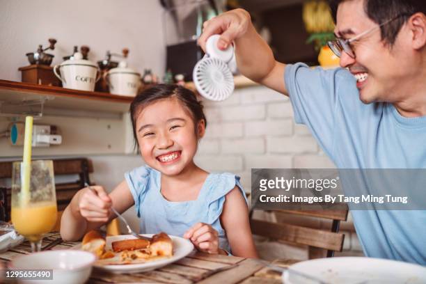 young handsome dad using a handheld electric fan to cool down her daughter while having meal in restaurant - cooling down stock-fotos und bilder