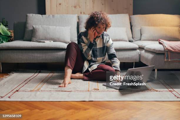 young businesswoman working from home: sitting on the floor, using her laptop and making a phone call - quarantine stock pictures, royalty-free photos & images