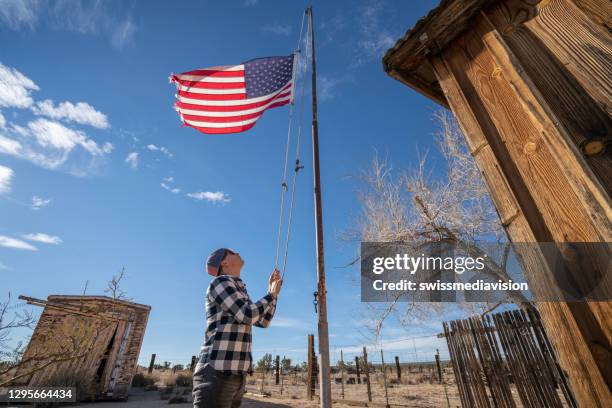 joven izando la bandera americana contra el cielo azul - asta fotografías e imágenes de stock