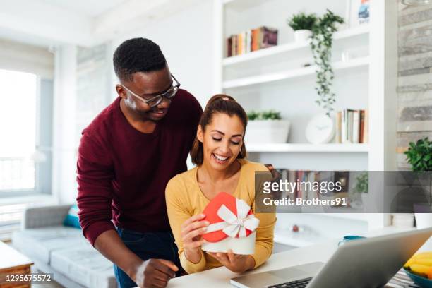 happy young and diverse couple celebrating valentine's day in their home - parcel laptop stock pictures, royalty-free photos & images