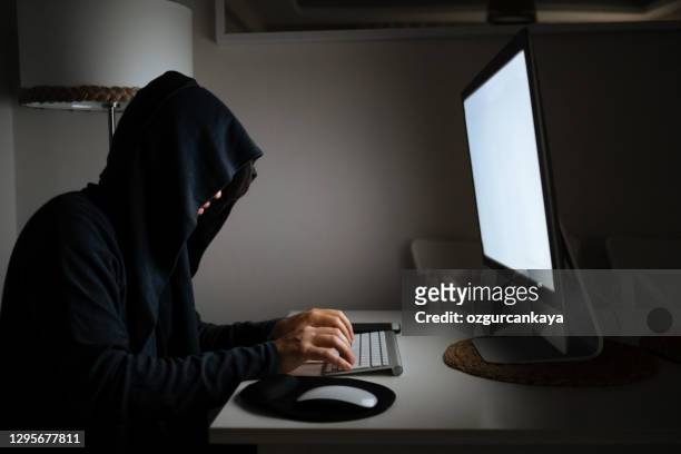uomo che indossa camicia con cappuccio e maschera usando laptop al buio per hackerare - uomo incappucciato foto e immagini stock