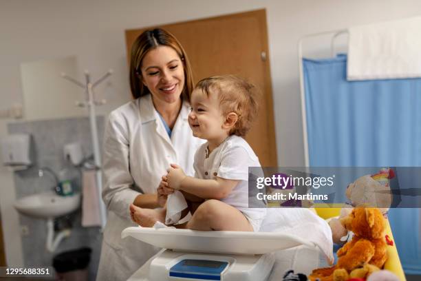 vrouwelijk kinderarts spelend met babyjongen op de lijst in artsenbureau - kinderarts stockfoto's en -beelden