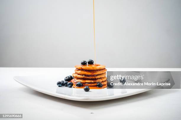 maple syrup falling on oatmeal pancakes with blueberries on a white plate - maple syrup pancakes fotografías e imágenes de stock