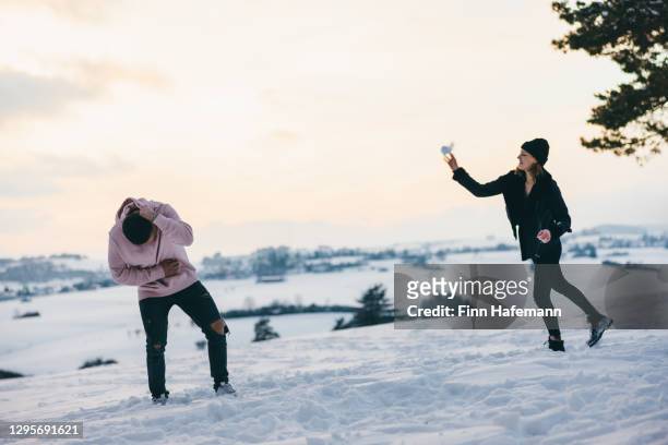 sneeuwbal gevecht in winter landschap jong paar met plezier - wegduiken stockfoto's en -beelden