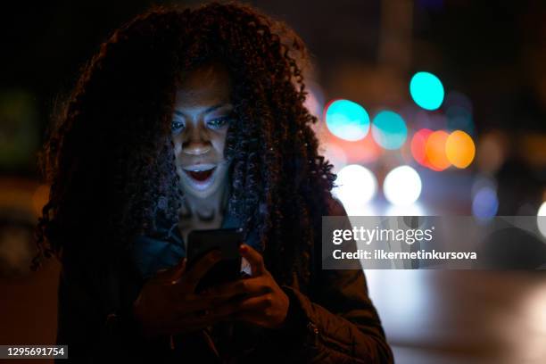 surprised woman reading bad news on her phone on street at night - mobile bad news stock pictures, royalty-free photos & images