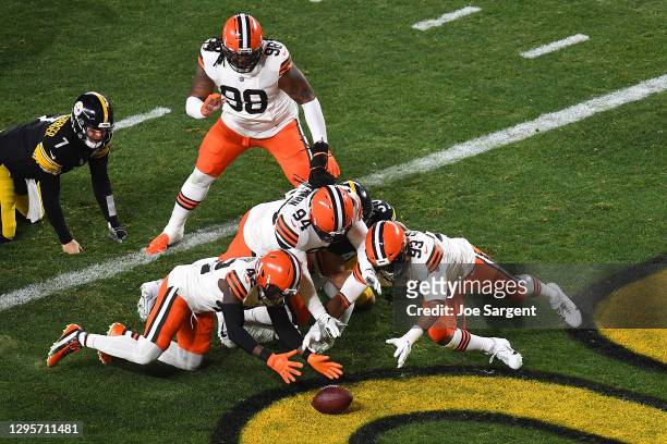Karl Joseph, B.J. Goodson and Adrian Clayborn of the Cleveland Browns dive for a loose ball during the first half of the AFC Wild Card Playoff game...
