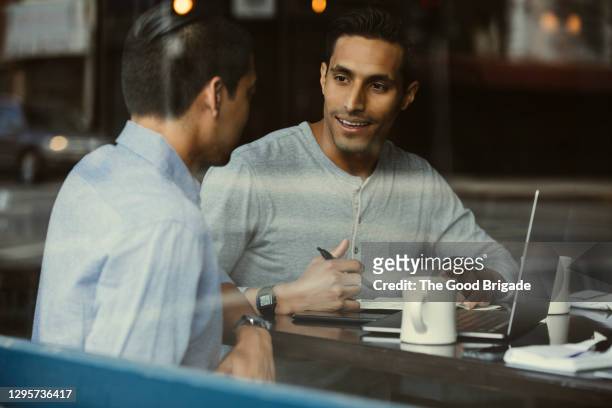 young businessman with laptop talking to colleague at table in cafe - cafe meeting stock pictures, royalty-free photos & images