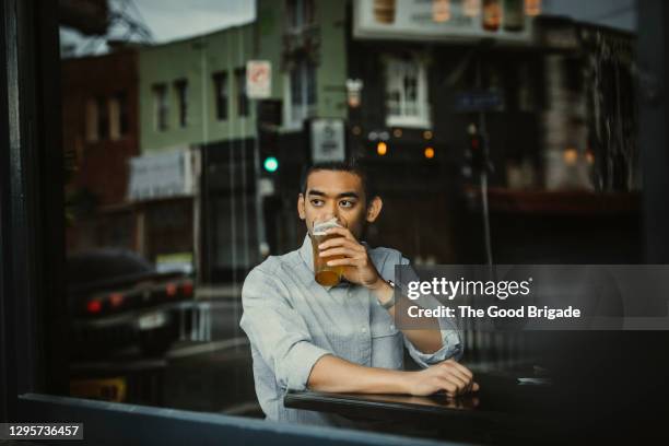 young man having beer while looking out of window in cafe - view-through-restaurant-window stock pictures, royalty-free photos & images