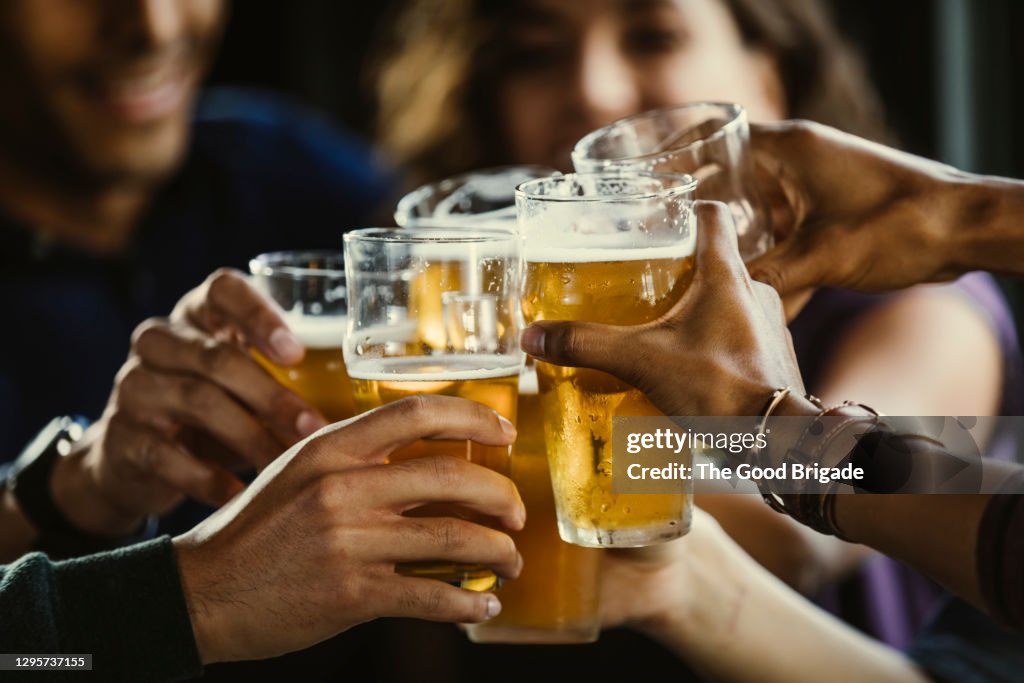 Group of friends toasting beer glasses at table in bar