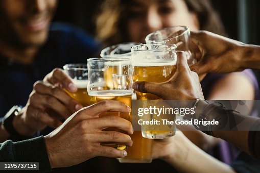 Group of friends toasting beer glasses at table in bar Group of friends toasting beer glasses at table in bar
