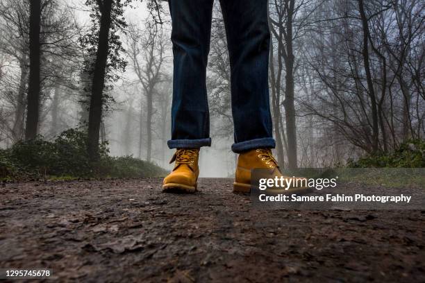 low section of a man, wearing boots and jean, standing on a footpath in forest. - laarzen geel stockfoto's en -beelden