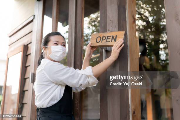 portrait shot of restaurant manager with face mask ,holding an open sign at the entrance as preparation to reopening post pandemic covid 19 - restaurant manager covid stock pictures, royalty-free photos & images