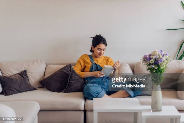 portrait of a young woman enjoying on the sofa and reading - girl reading stock pictures, royalty-free photos & images