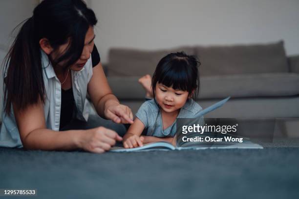 mother reading a book to her daughter on carpet - china foto e immagini stock