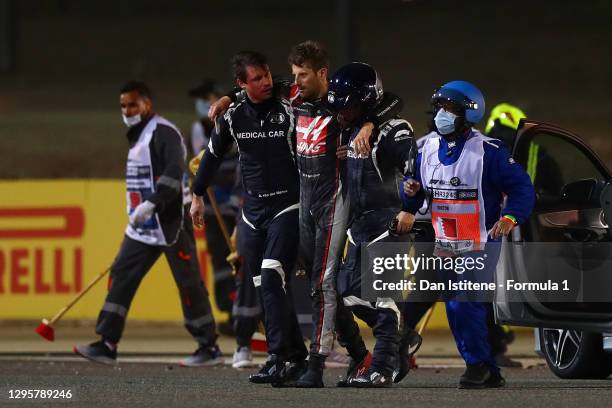 Romain Grosjean of France and Haas F1 is helped to a waiting ambulance by the FIA medical car driver Alan van der Merwe and FIA medical rescue...